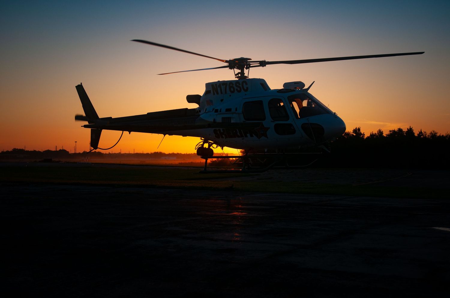 Silhouette of helicopter against dramatic orange sunset sky.