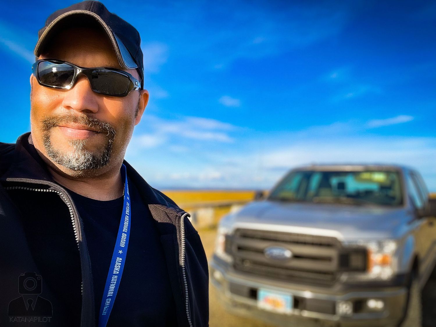 Pickup truck parked against blue sky and tundra landscape backdrop.