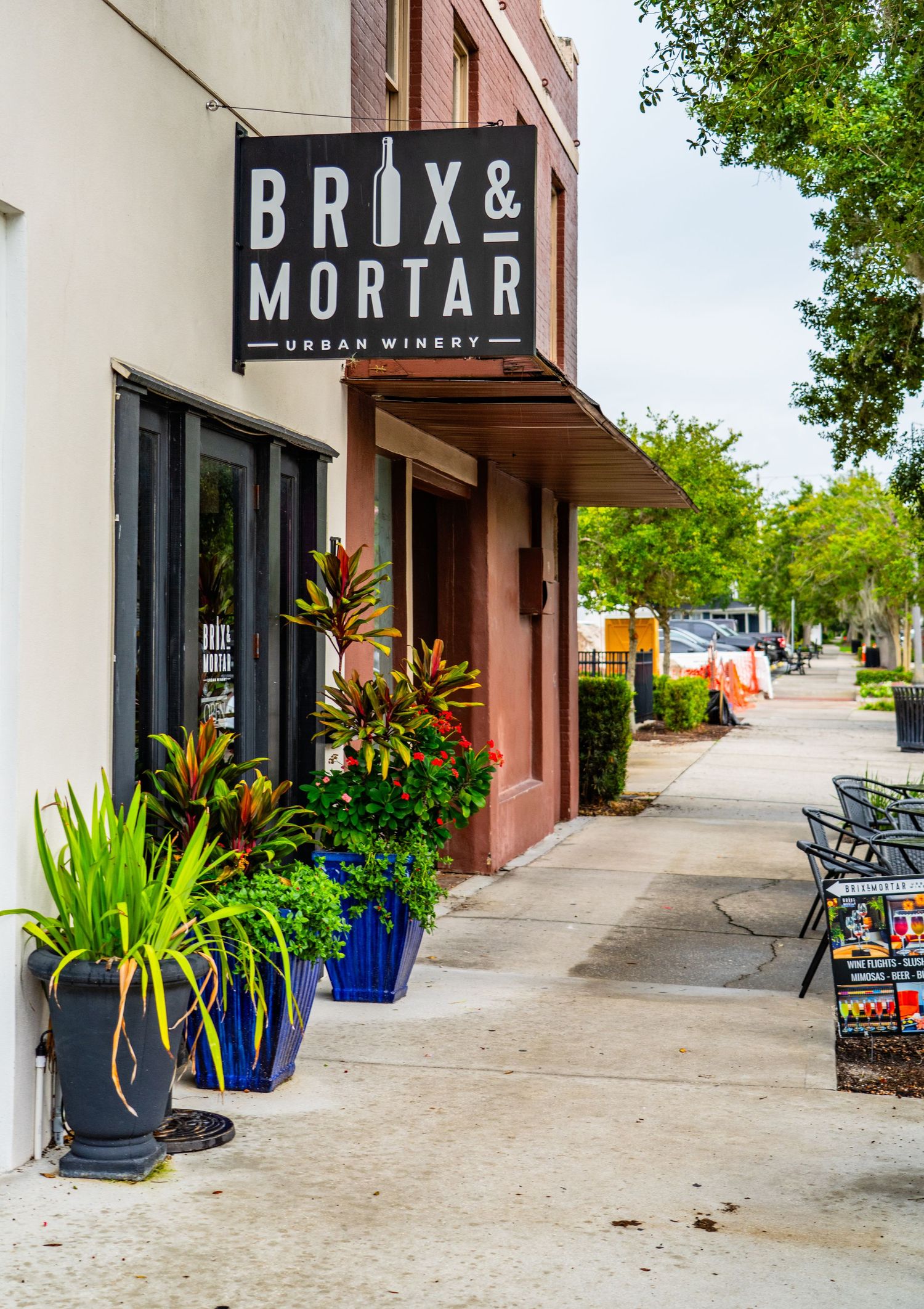 Storefront of Brix & Mortar shop with decorative blue planters filled with colorful plants along the sidewalk.