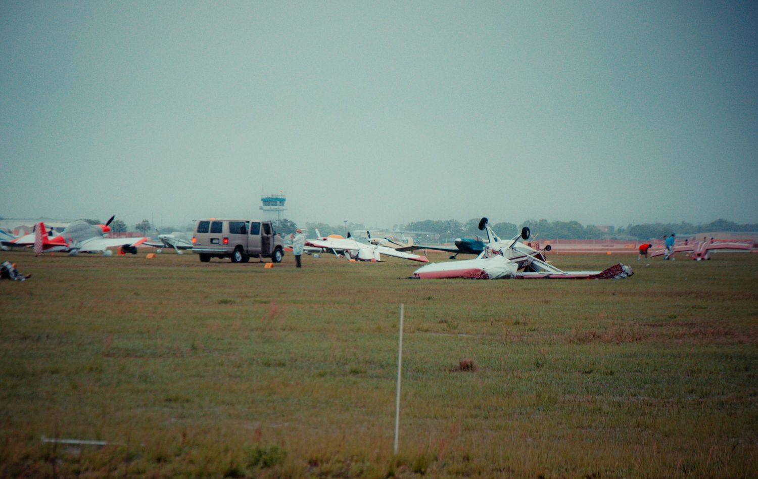 Panoramic view of a rural airfield with small aircraft parked on the grass under an overcast sky.