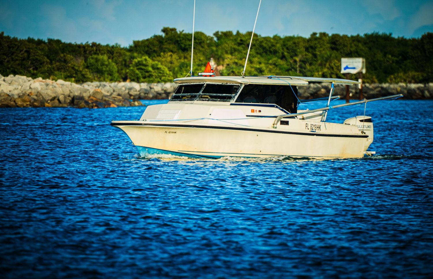 A series of boats cruising on blue rippling water against a shoreline with trees on a sunny day.