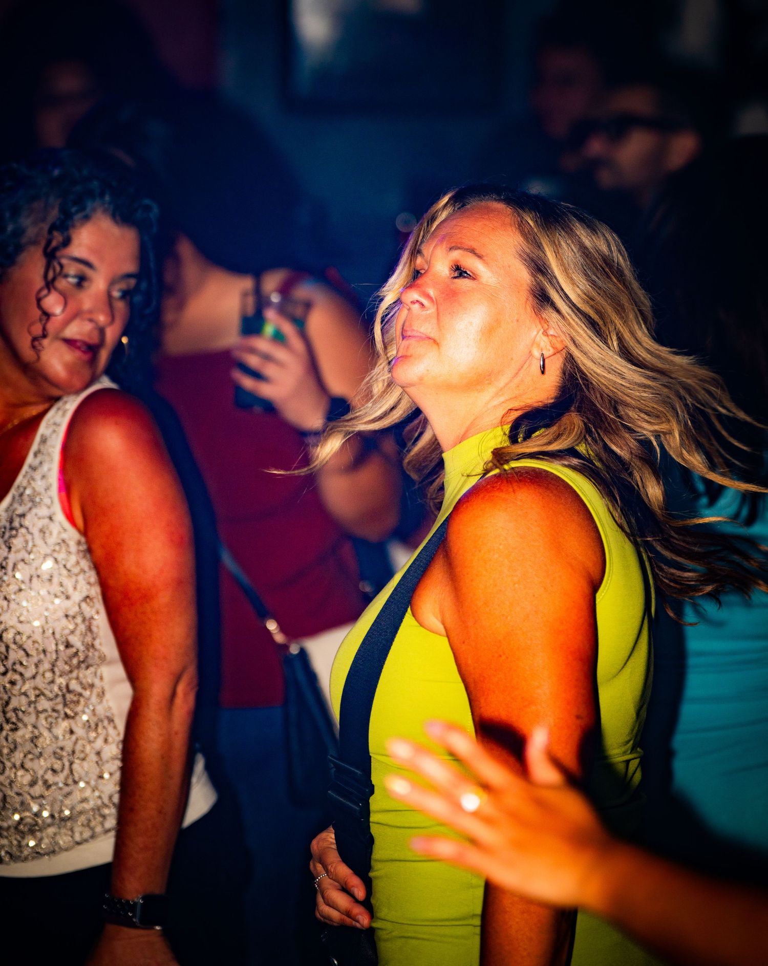 Energetic dance floor scene with partygoers in bright outfits under club lighting.