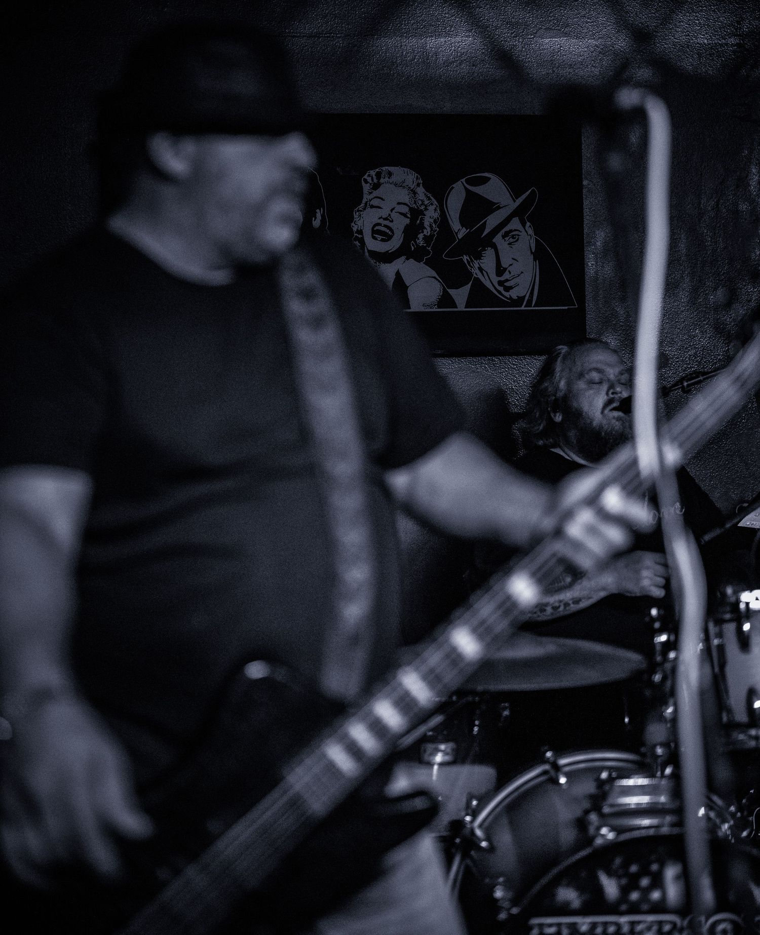 Black and white photo of musicians performing with drums and guitar on stage.