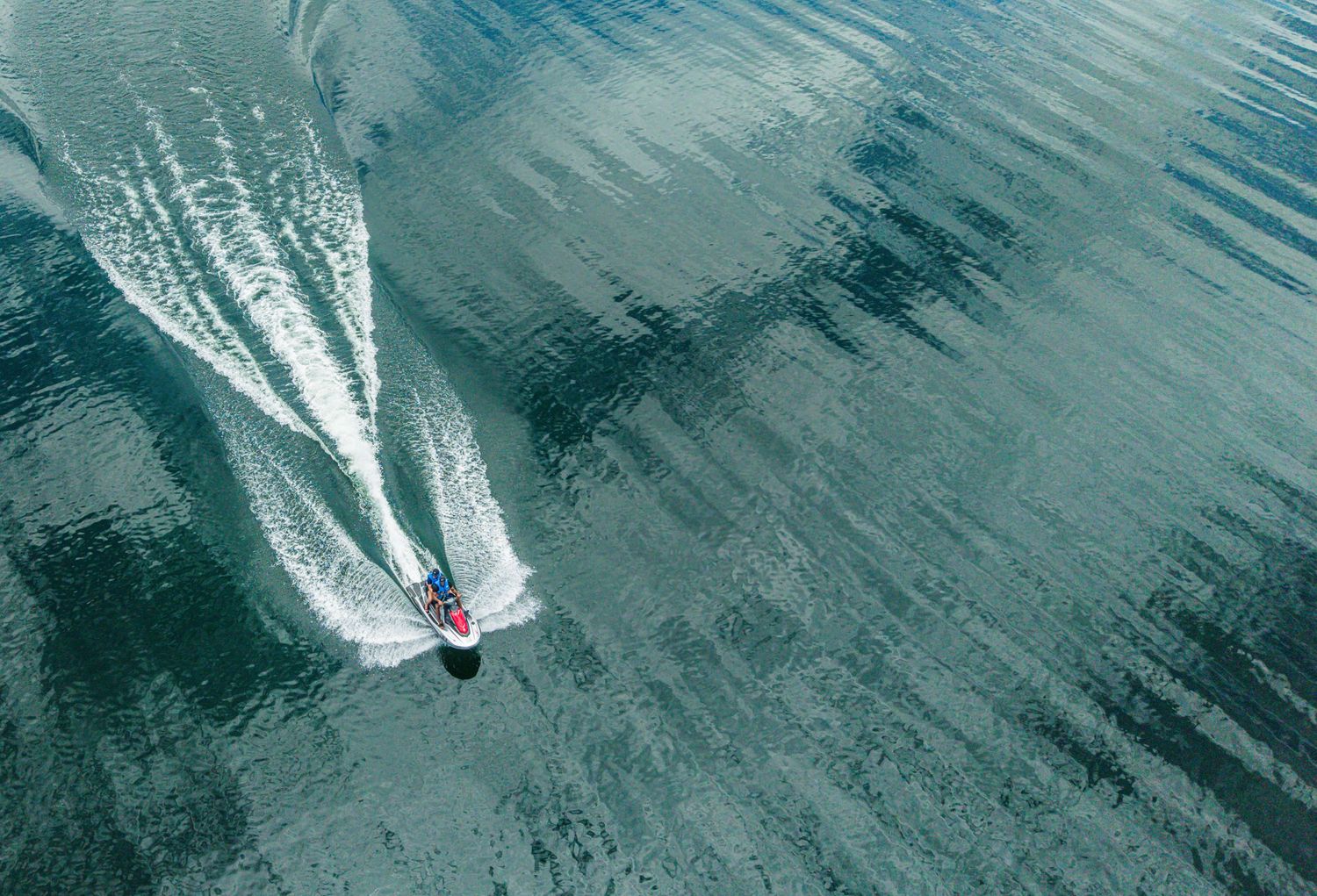Aerial view of a red speedboat cutting through calm teal waters, leaving a white wake trail behind.