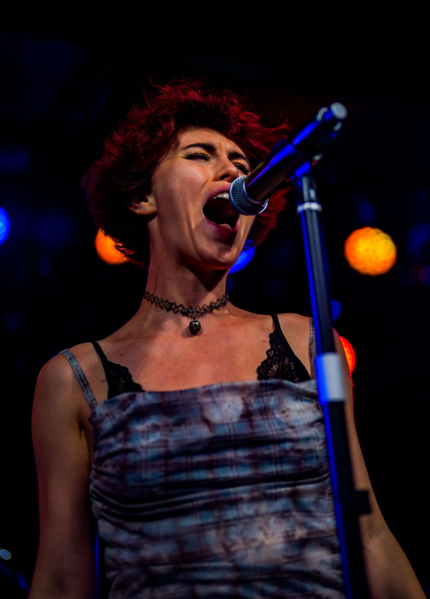 Red-haired female vocalist singing passionately into a microphone on a live stage.