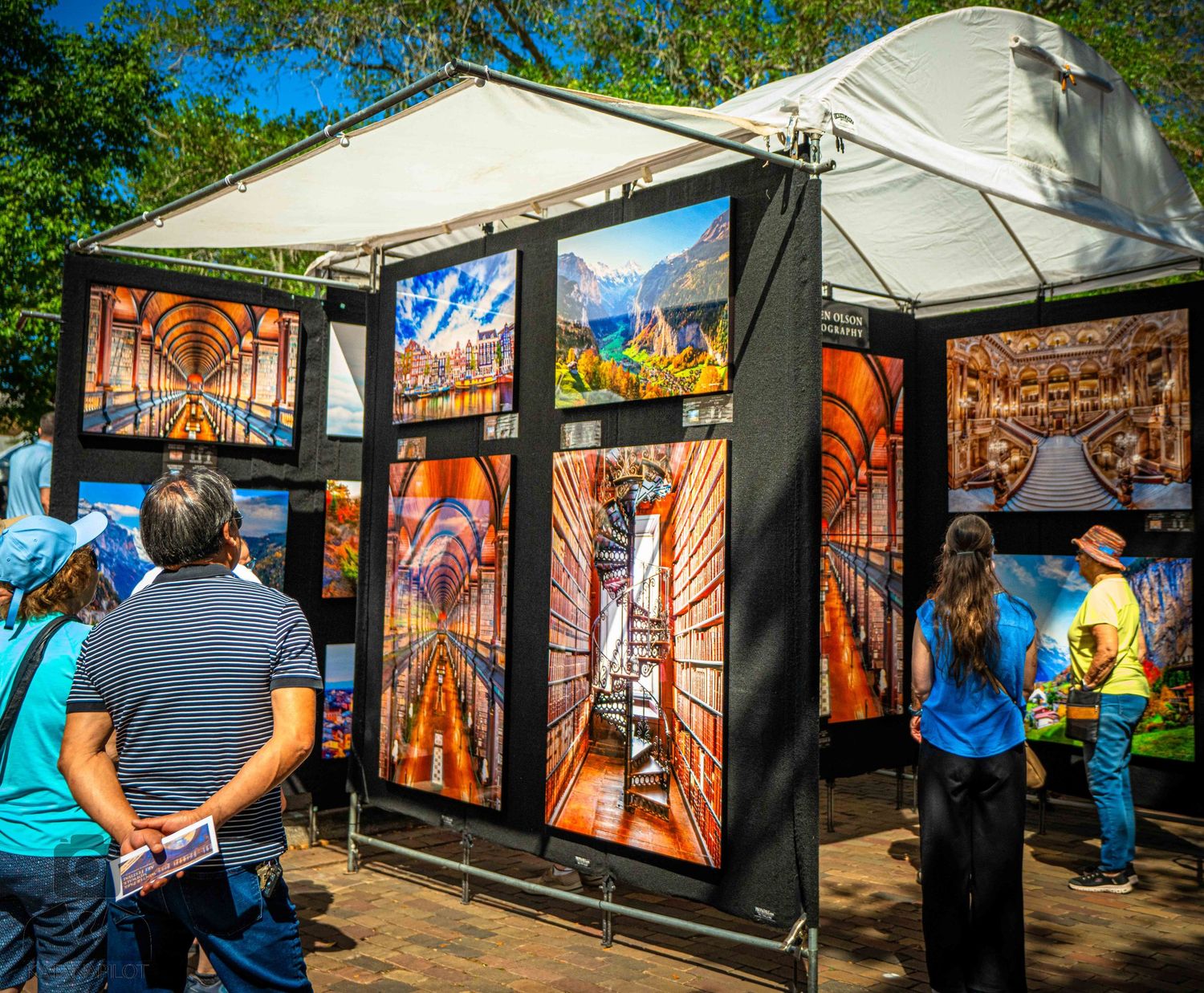 Art vendor booth displaying colorful photography prints in a white tent at an outdoor festival.