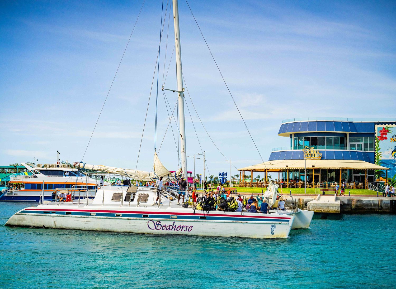 Seahorse catamaran sailboat docked at a colorful Caribbean marina with tourists on board.