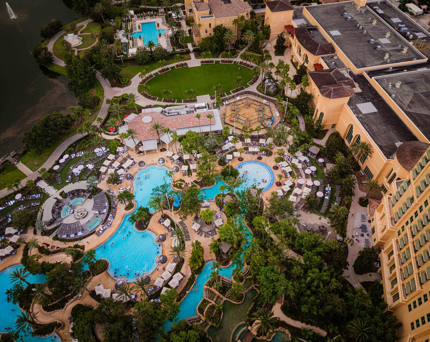 Aerial view of a luxury resort with winding lazy river, multiple pools, lounge chairs, and lush tropical landscaping.