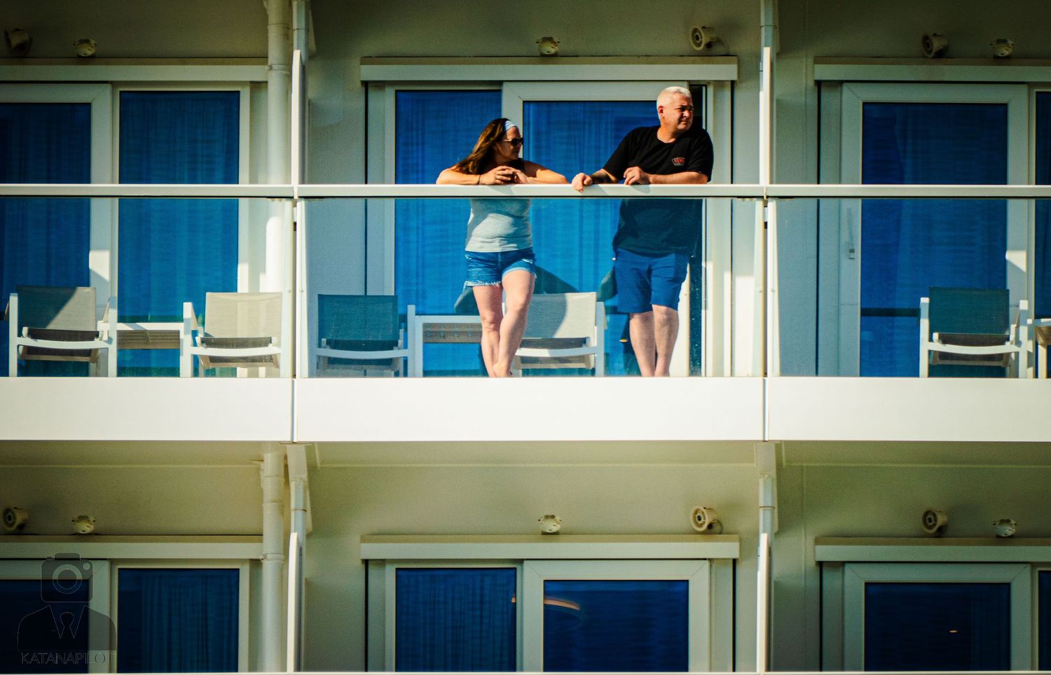 Modern cruise ship balconies and windows reflect sunlight against a bright blue sky.