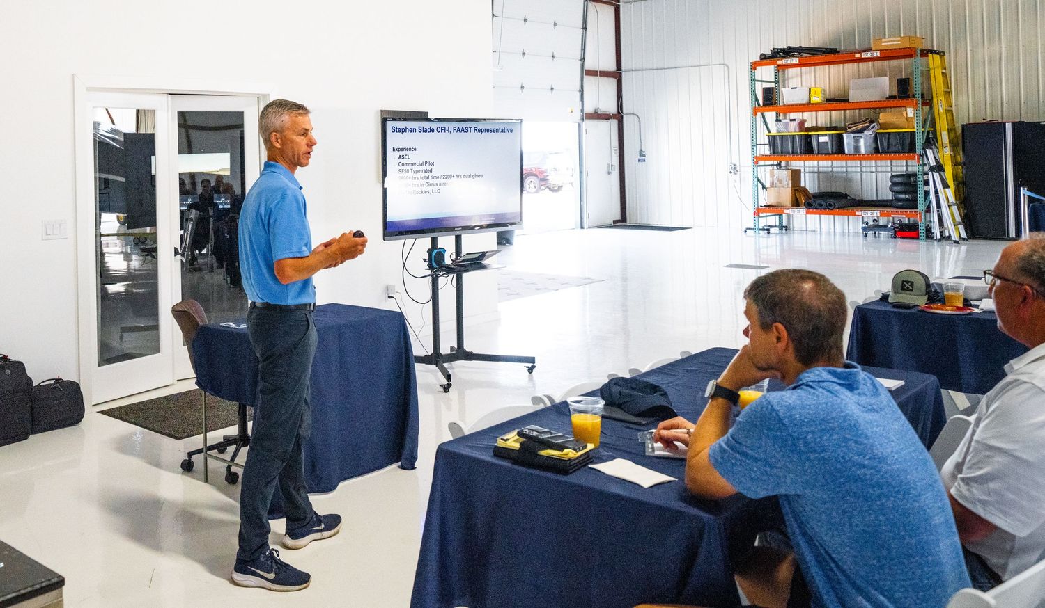 Side view of attendees watching a presentation on wall-mounted screens in an industrial space.