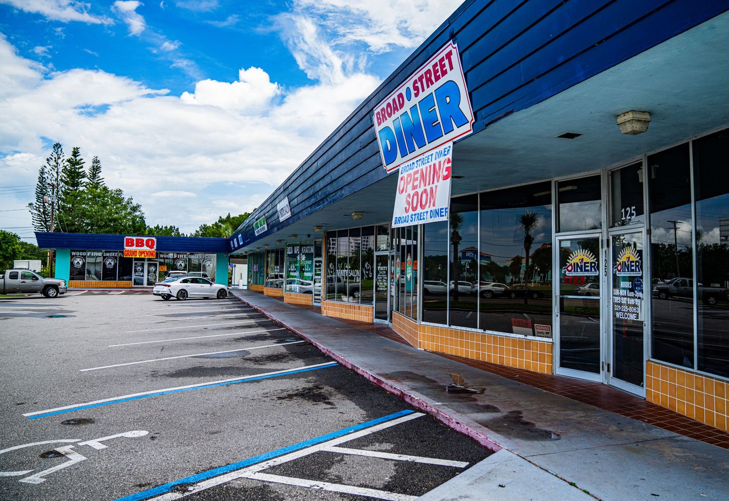 Strip mall storefront with blue awning and empty parking spaces on a cloudy day.