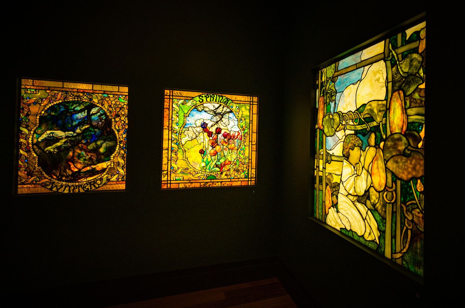 Series of backlit stained glass panels arranged horizontally in a museum exhibition space.