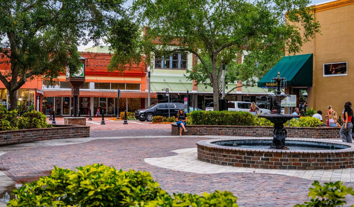 Tree-lined plaza with brick pavers and landscaping in a downtown shopping area.