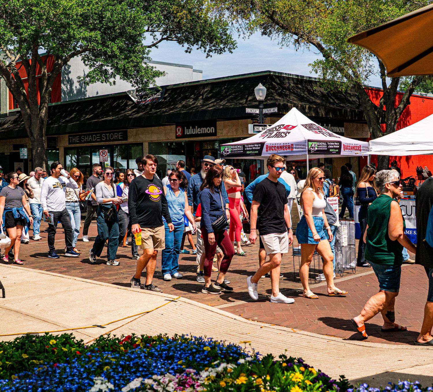 Crowded outdoor marketplace with people walking between vendor stalls under sunny skies.