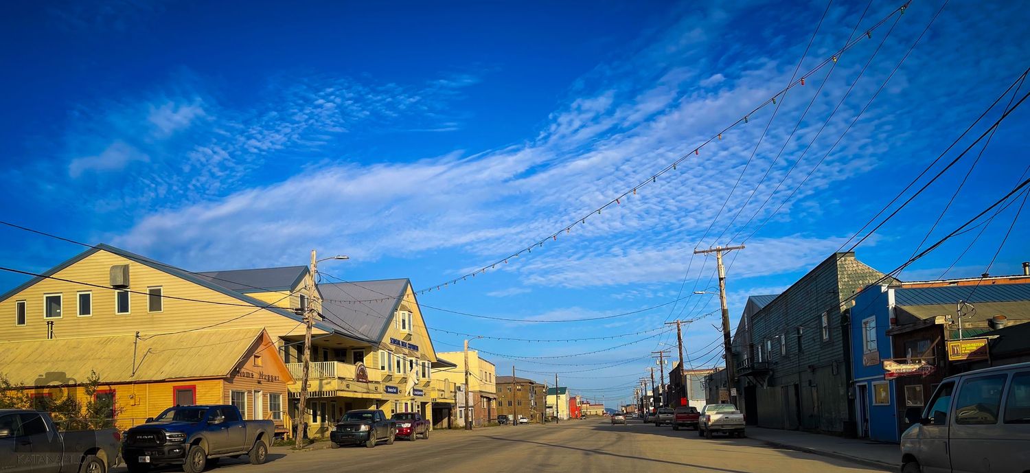 Panoramic view of a small town's main street with buildings under bright blue sky.