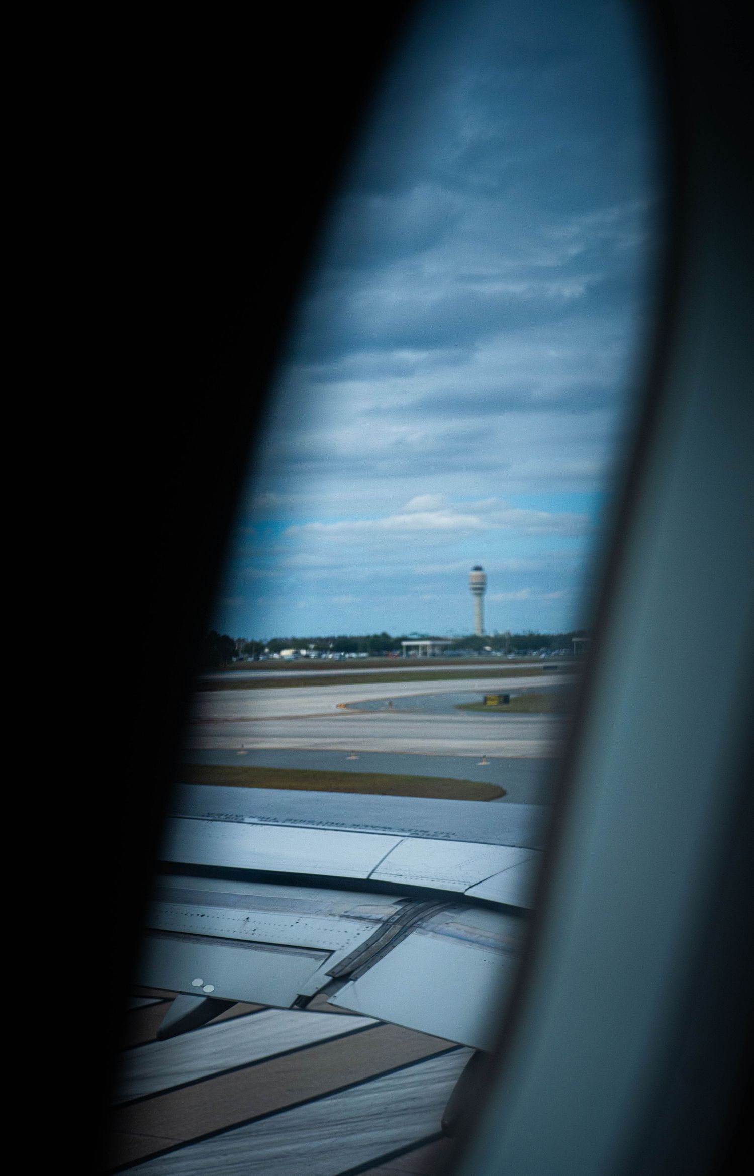 View from airplane window showing aircraft wing and airport control tower against blue sky.