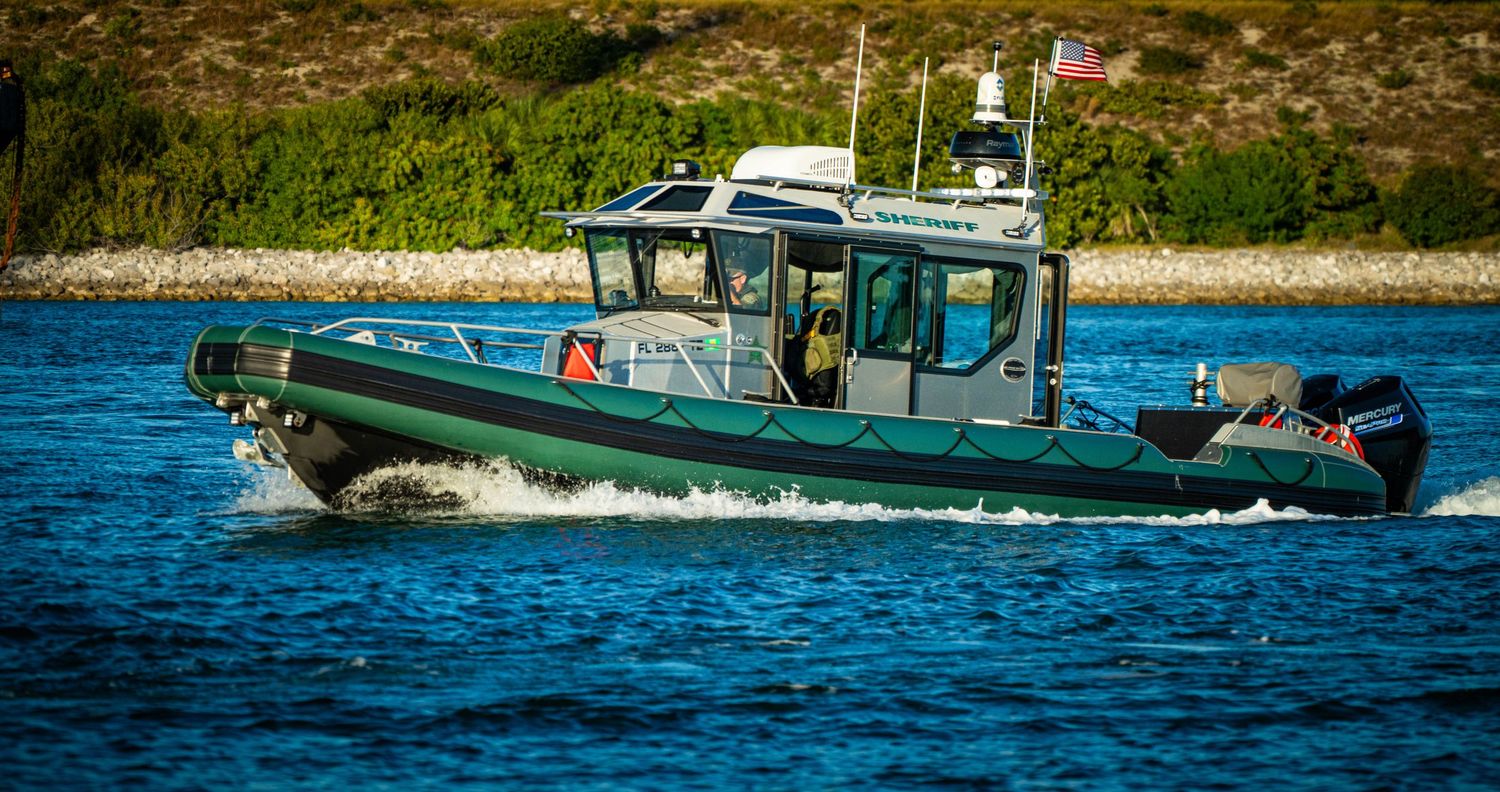 A blue and white patrol boat cruises through calm waters near a rocky coastline.