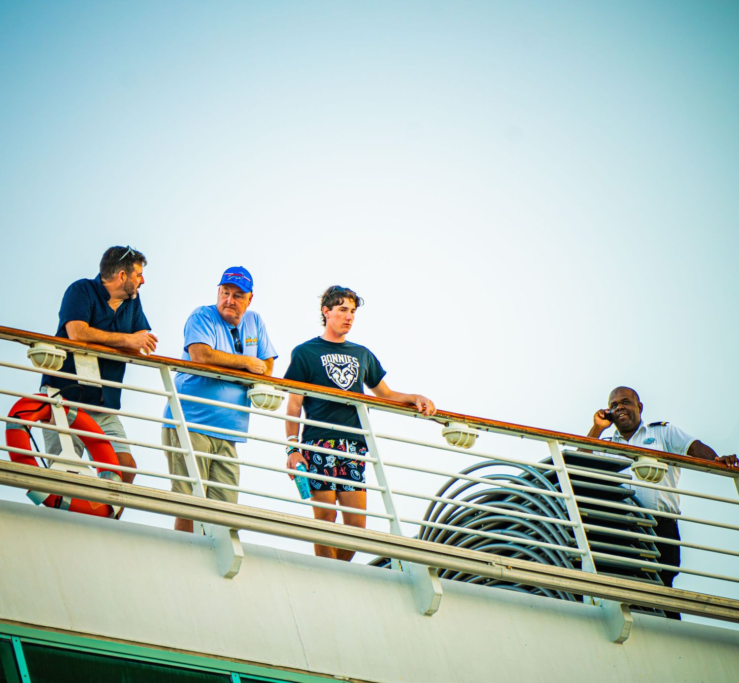 A group of people lean over the railing of a boat deck to observe something in the water below.