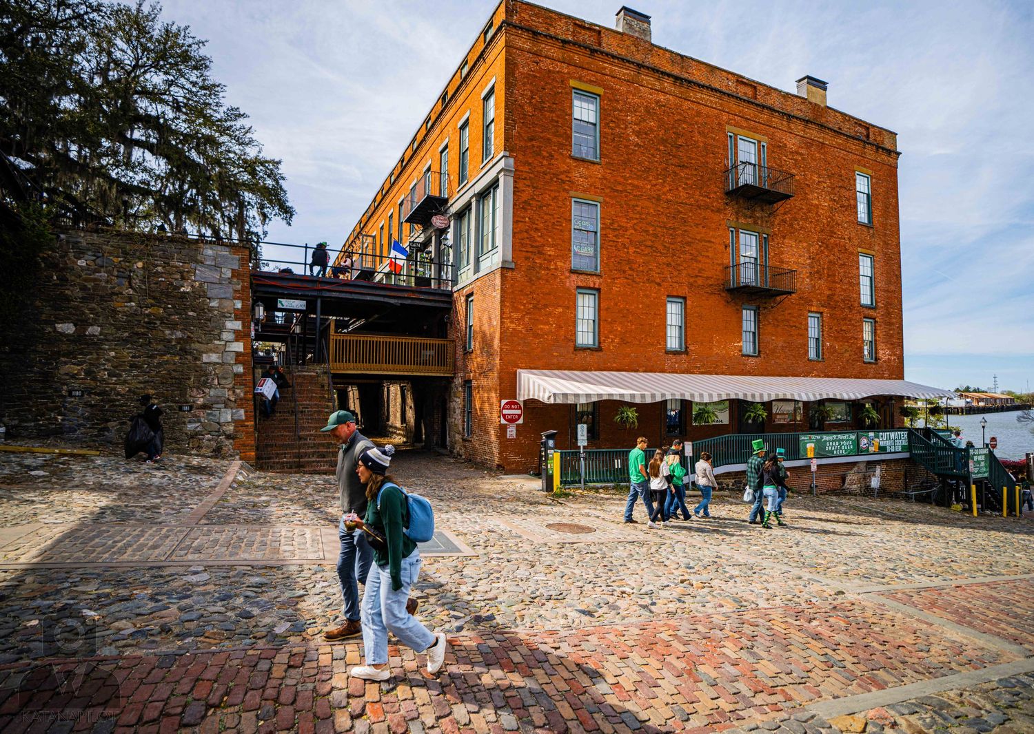 Orange brick building with stone foundation on a hilltop against blue sky with people walking outside.