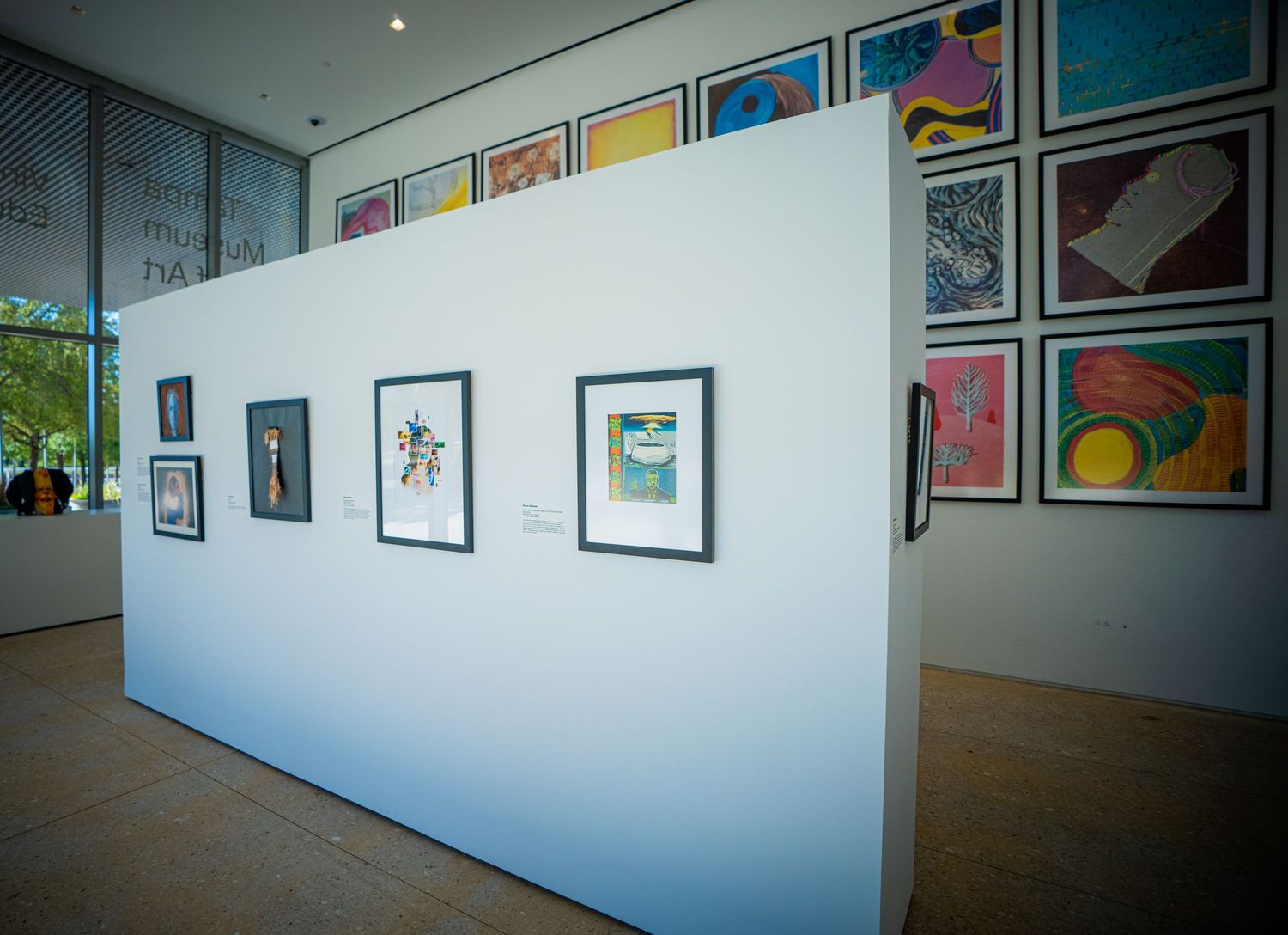 Art gallery interior showing multiple framed artworks displayed along white walls in a modern exhibition space.