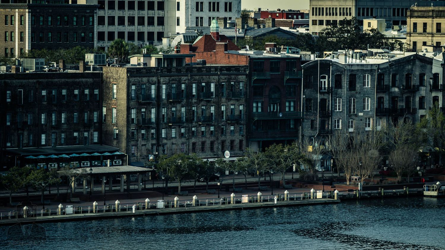 Panoramic cityscape view of historic buildings along a waterfront with boats and industrial architecture.