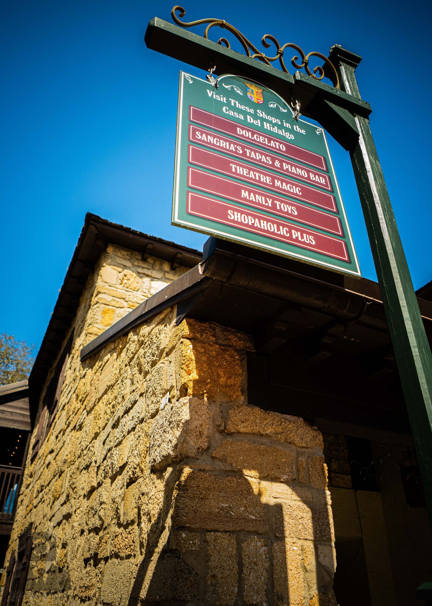 Rustic stone wall building with wooden signage against deep blue sky in historic district.