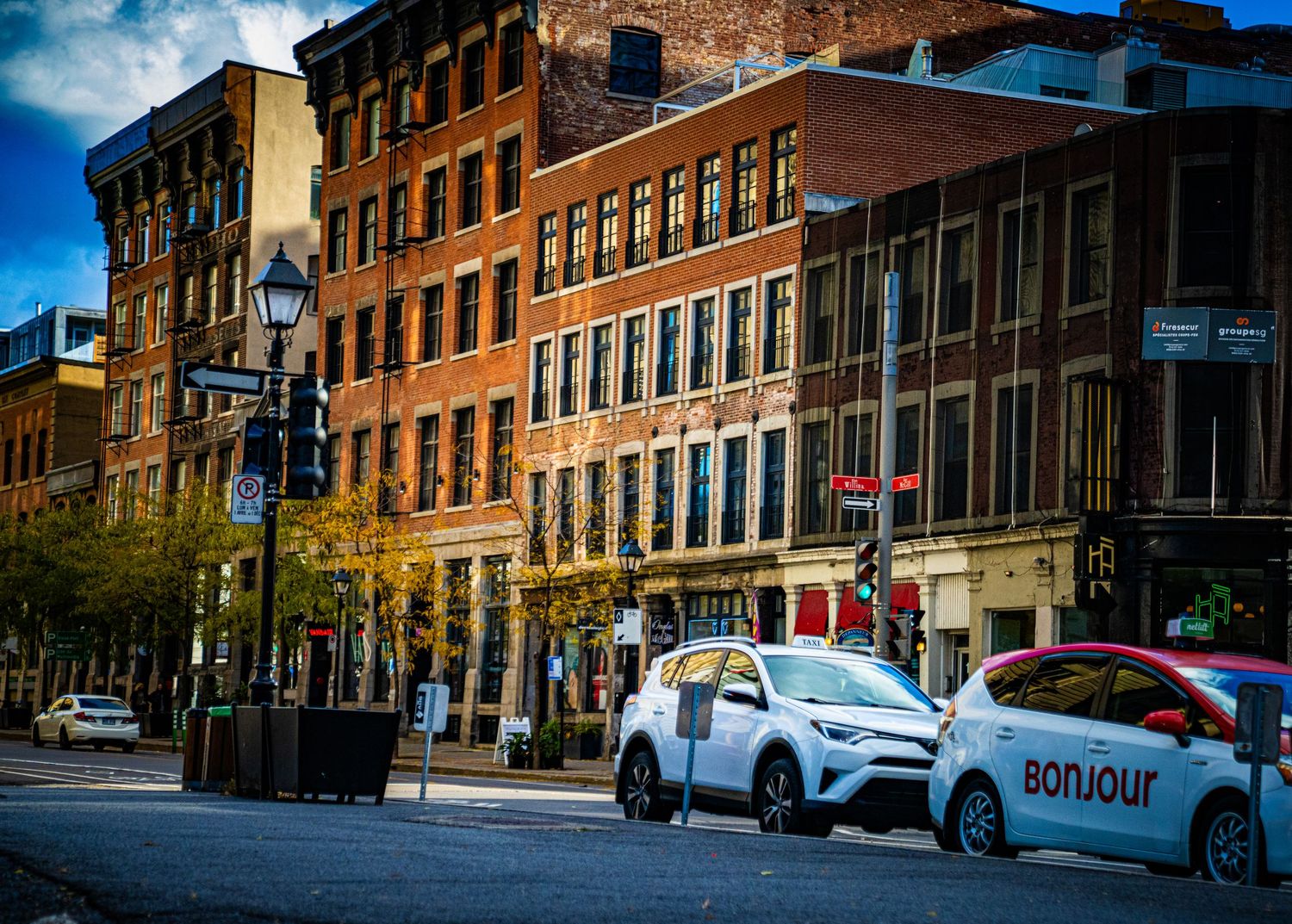 Historic brick buildings line a cobblestone street in an old city district on a sunny day.