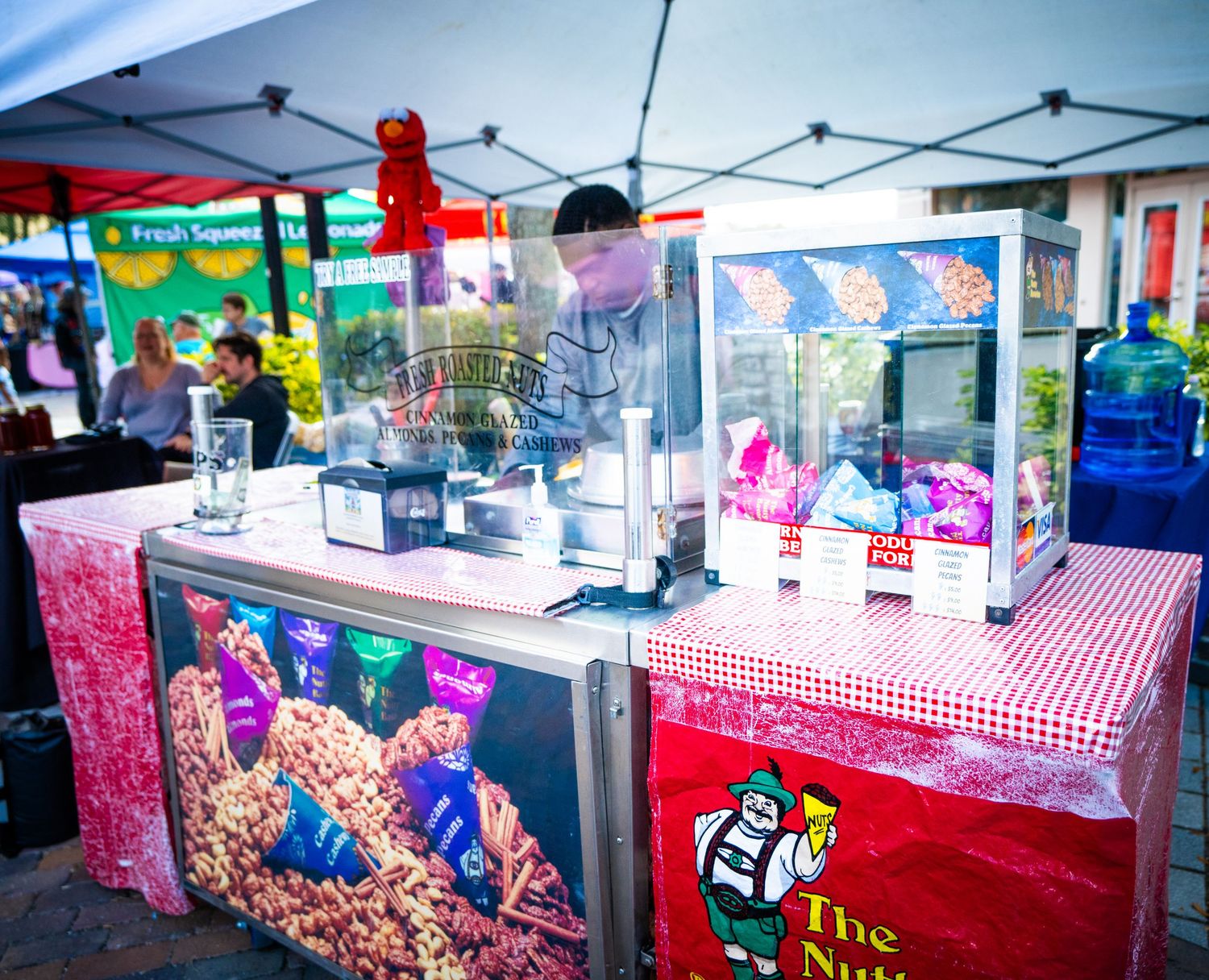 Colorful vendor booths with red and white checkered tablecloths line up at an outdoor market or festival event.