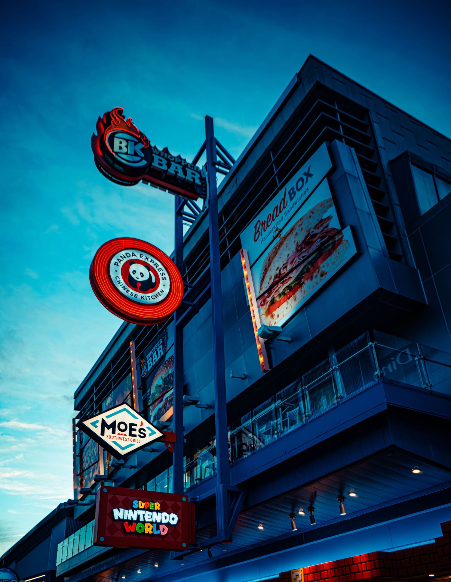 A row of illuminated storefront signs glowing in blue twilight with circular red Panda Express and Target logos visible.