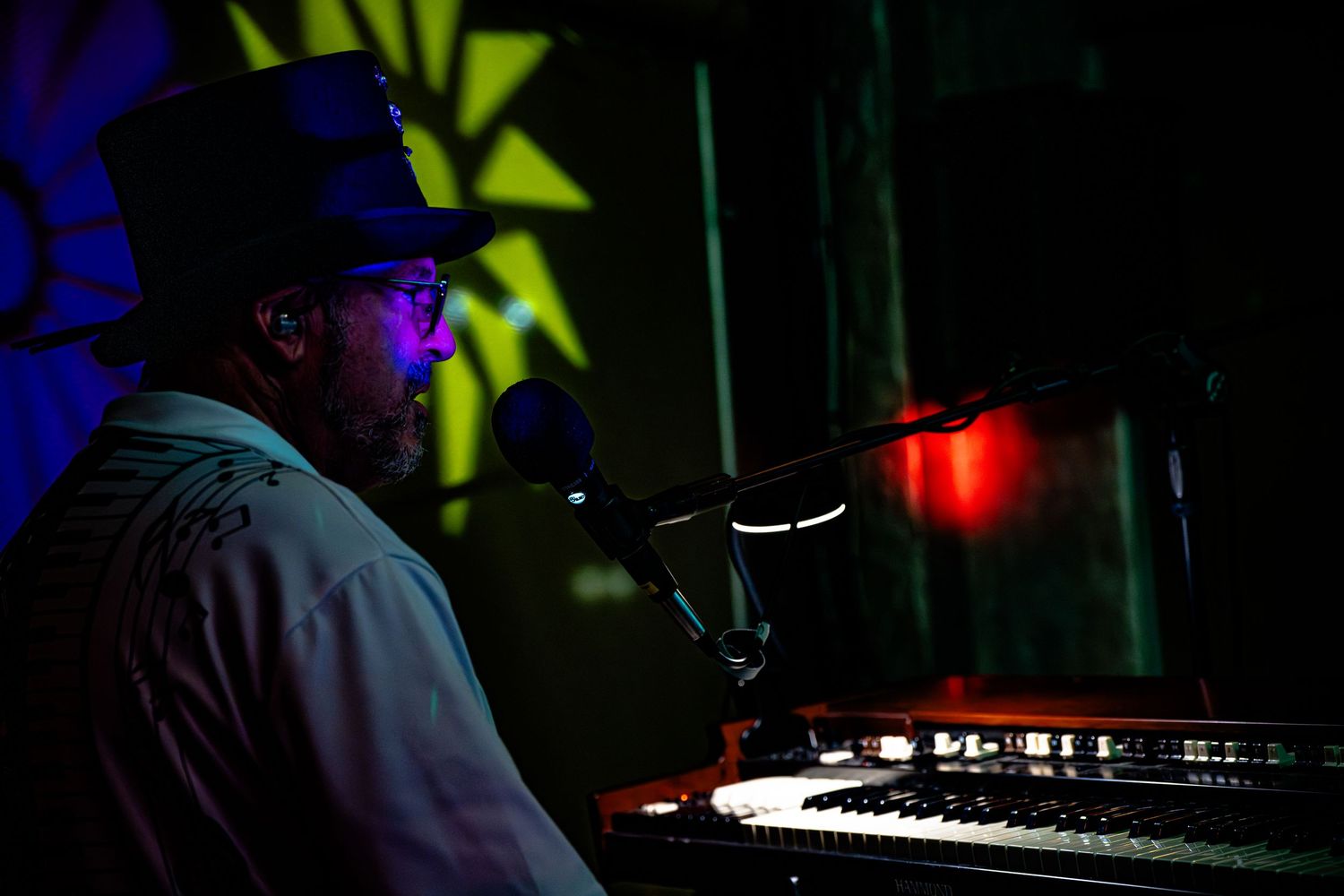 A musician performing at a keyboard station with dramatic red lighting and star decorations in the background.
