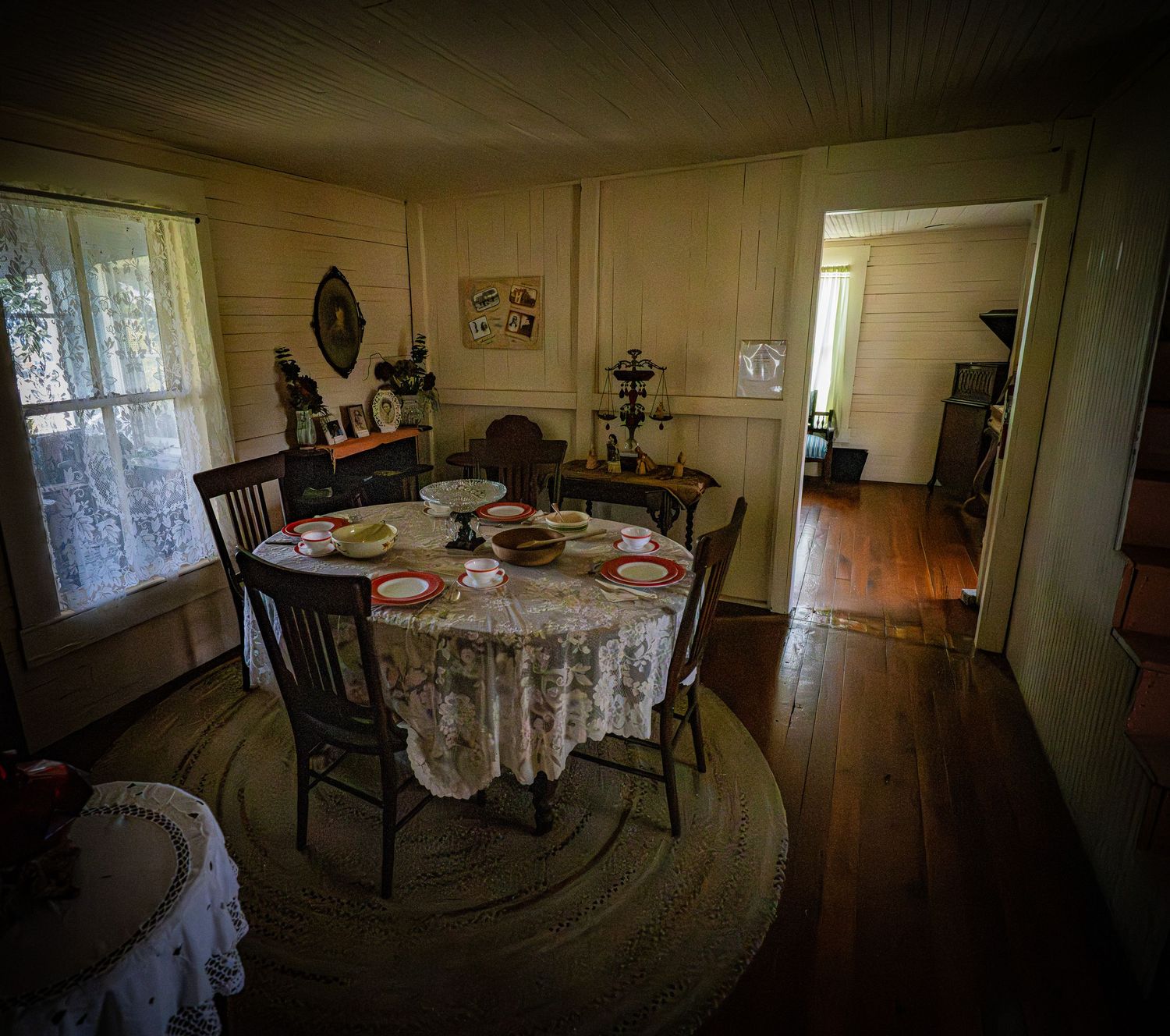 Vintage dining room with lace tablecloth, wooden chairs, and period decorations in warm lighting.
