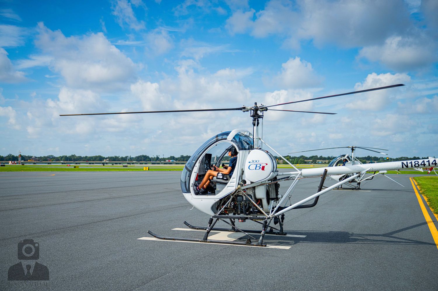 White helicopter with red accents sits on runway with green fields in background.