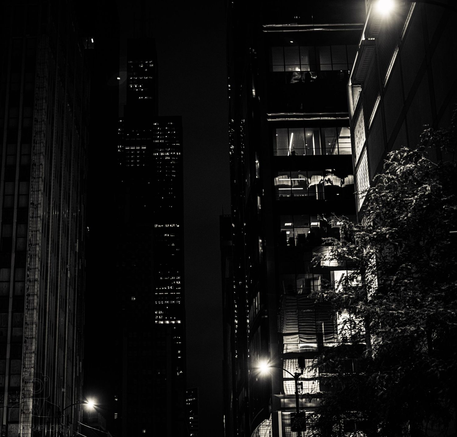 Urban night scene with tall buildings and bright lights creating dramatic contrasts.