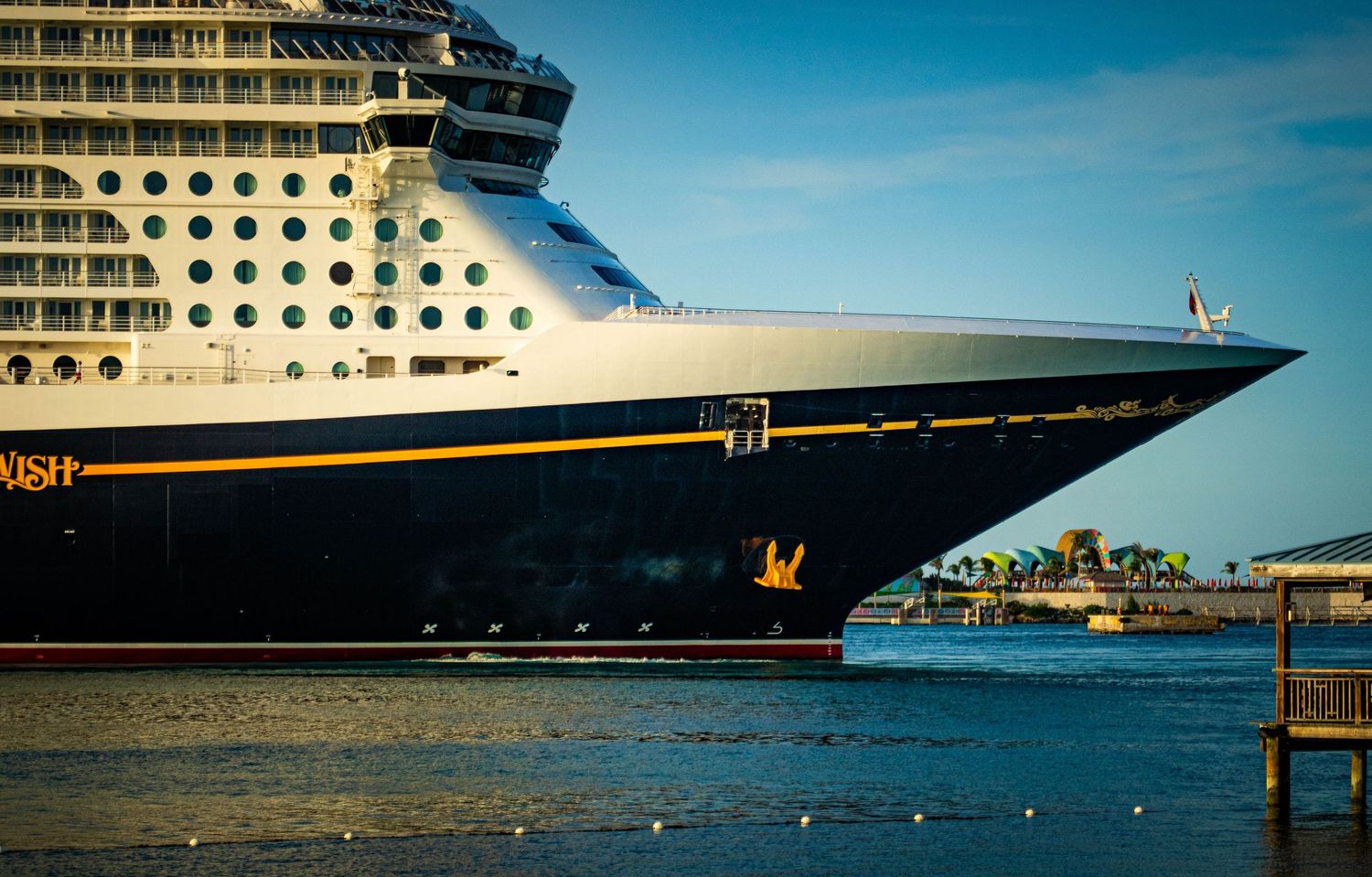 Disney Wish cruise ship docked at port, showcasing its massive bow and iconic gold detailing on calm waters.
