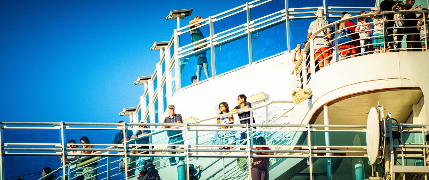 Cruise ship passengers enjoy the upper deck amenities and ocean views under bright blue skies.
