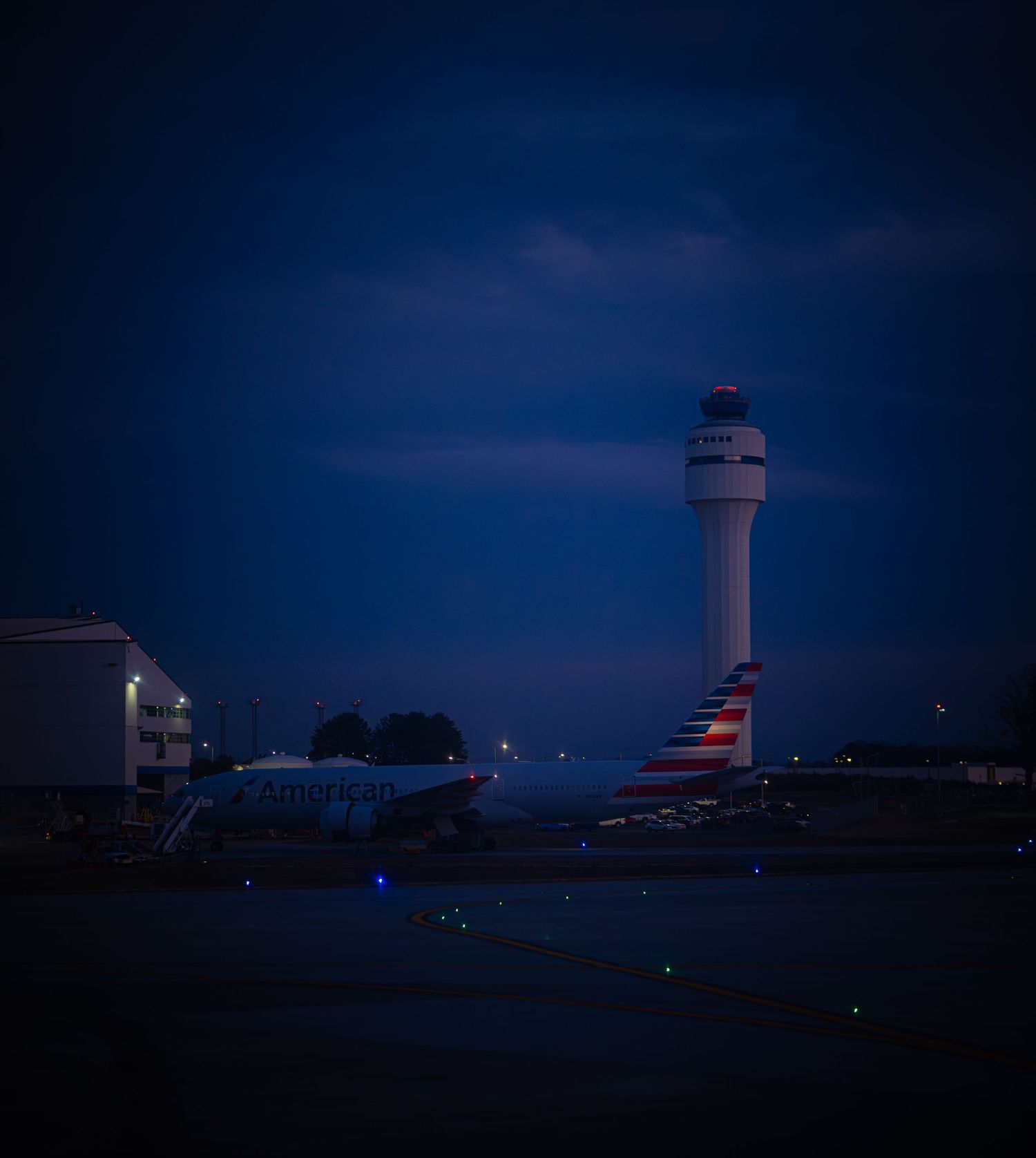Airport control tower and terminal buildings silhouetted against a deep blue twilight sky with scattered lights.