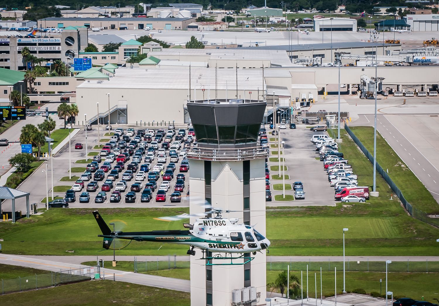 Airport control tower overlooking parking lot filled with vehicles.