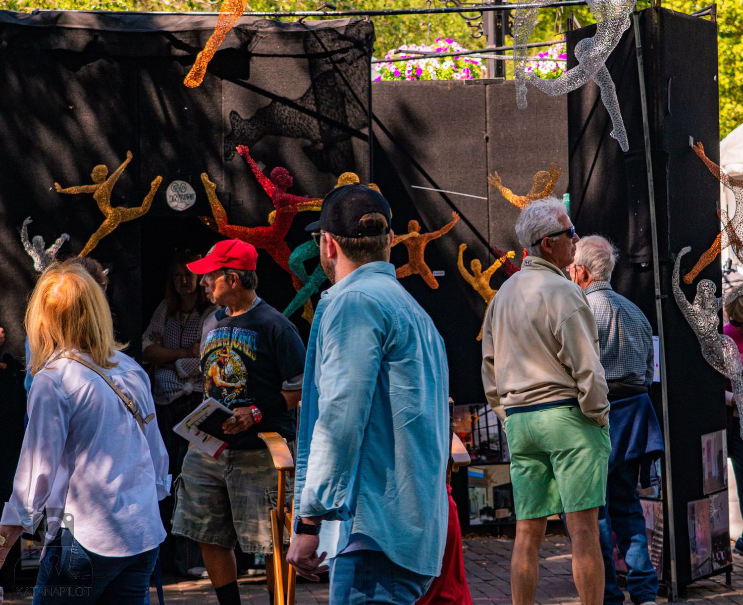 Festival attendees browsing artwork displays under shaded canopies.
