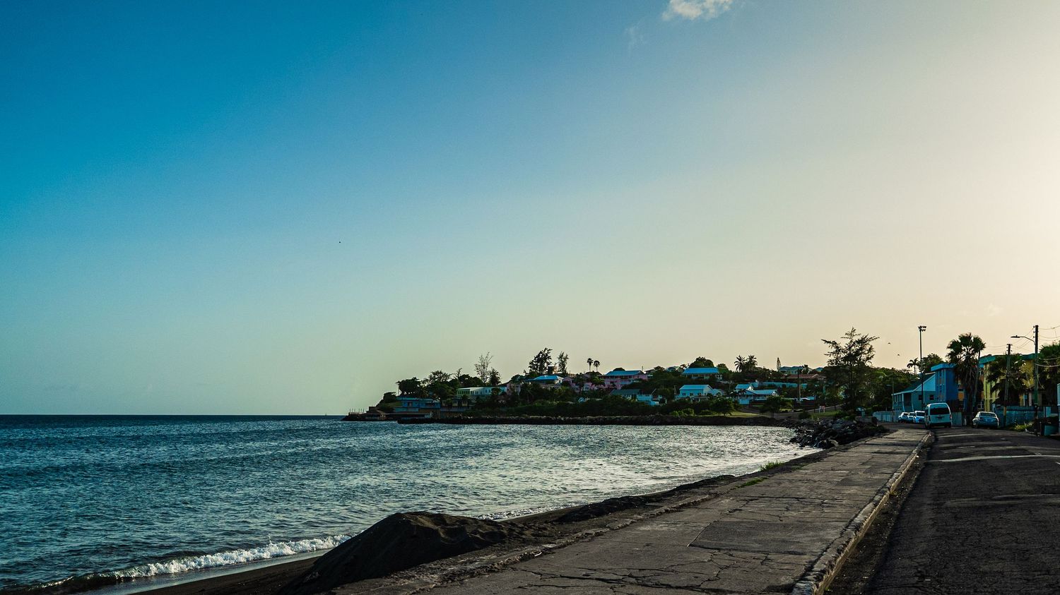 Scenic coastal landscape with palm trees and beachfront buildings under a vibrant blue sky.