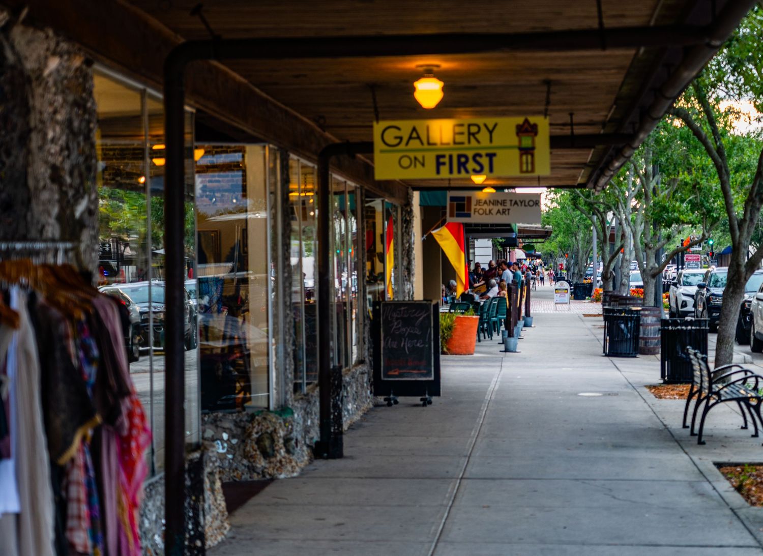 Covered shopping arcade with retail storefronts and clothing racks along a pedestrian walkway.