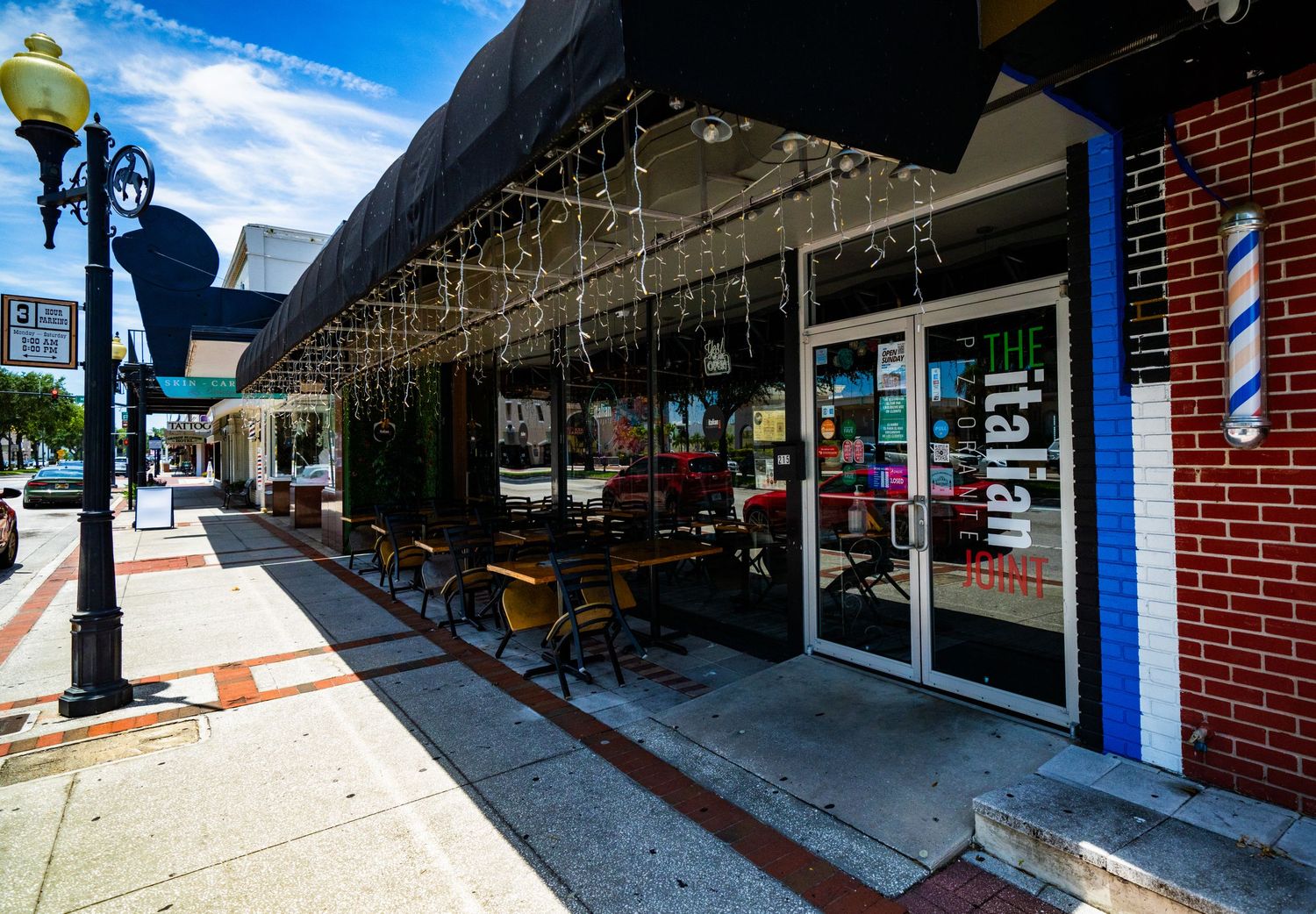Wide angle view of retail storefronts with covered sidewalk and brick architecture.