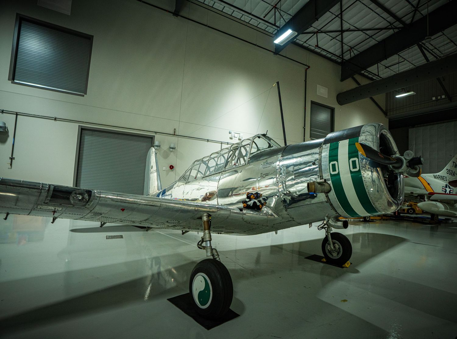Polished chrome vintage military trainer aircraft displayed inside a museum hangar with green stripe markings.