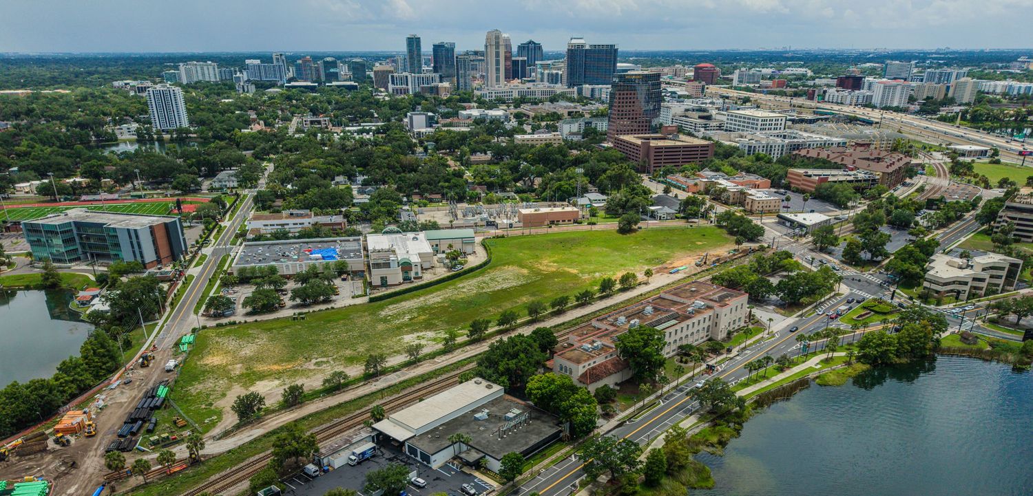 Aerial view of Orlando, Florida skyline with green parks, railway tracks, and a shimmering lake on a sunny day.