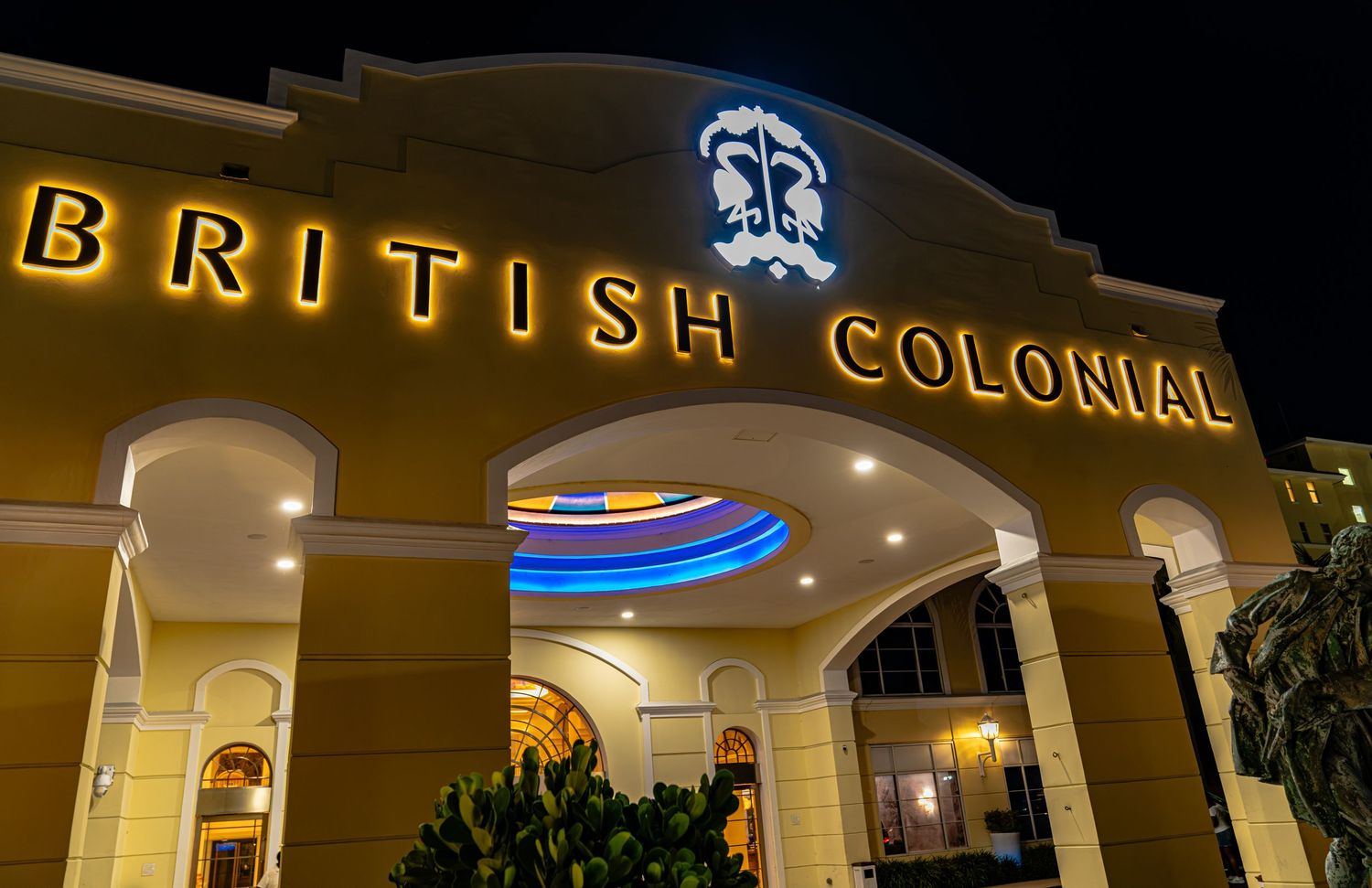 Illuminated British Colonial hotel sign glowing at night with elegant architecture and arched entrance in warm golden lights.