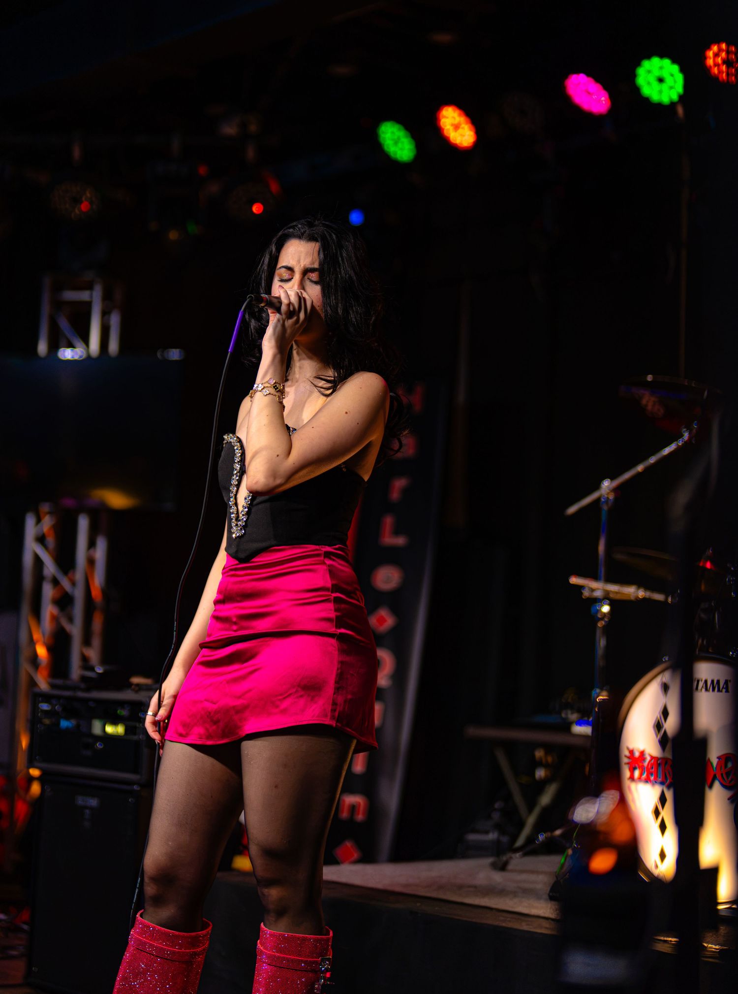 Female singer in pink skirt and corset top performing on stage under colorful lights at a Hard Rock venue.