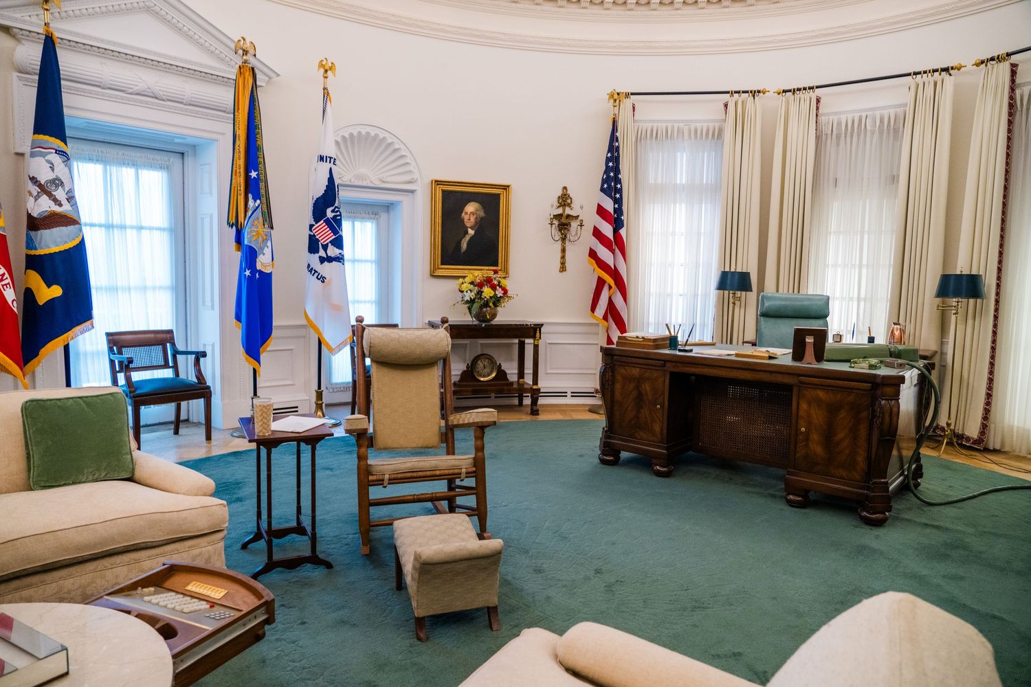 Formal office interior with blue carpet, American flags, and traditional furnishings.