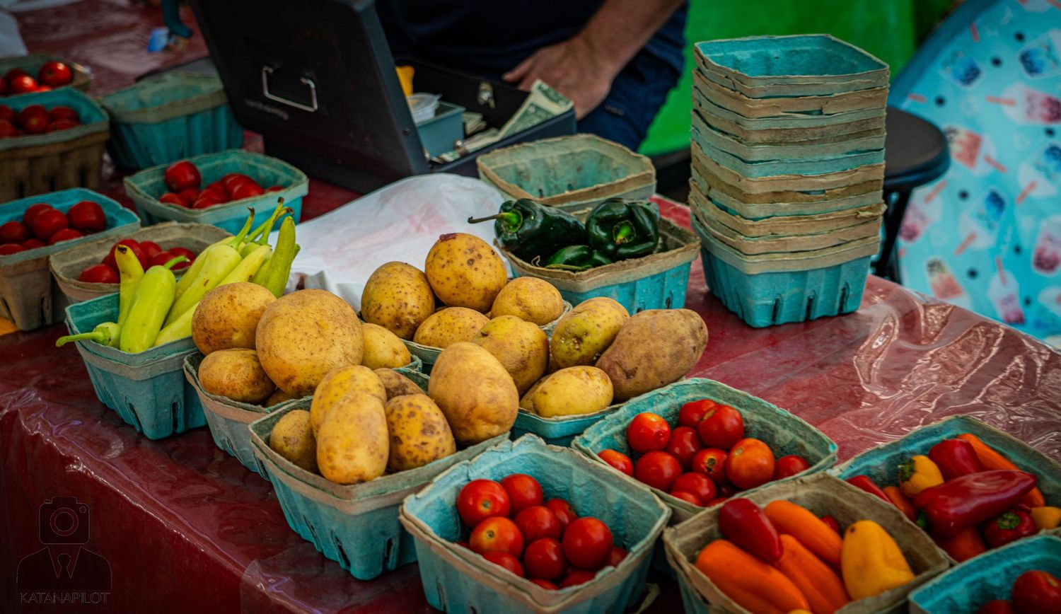 Fresh produce display featuring yellow potatoes, cherry tomatoes and other vegetables in turquoise baskets.