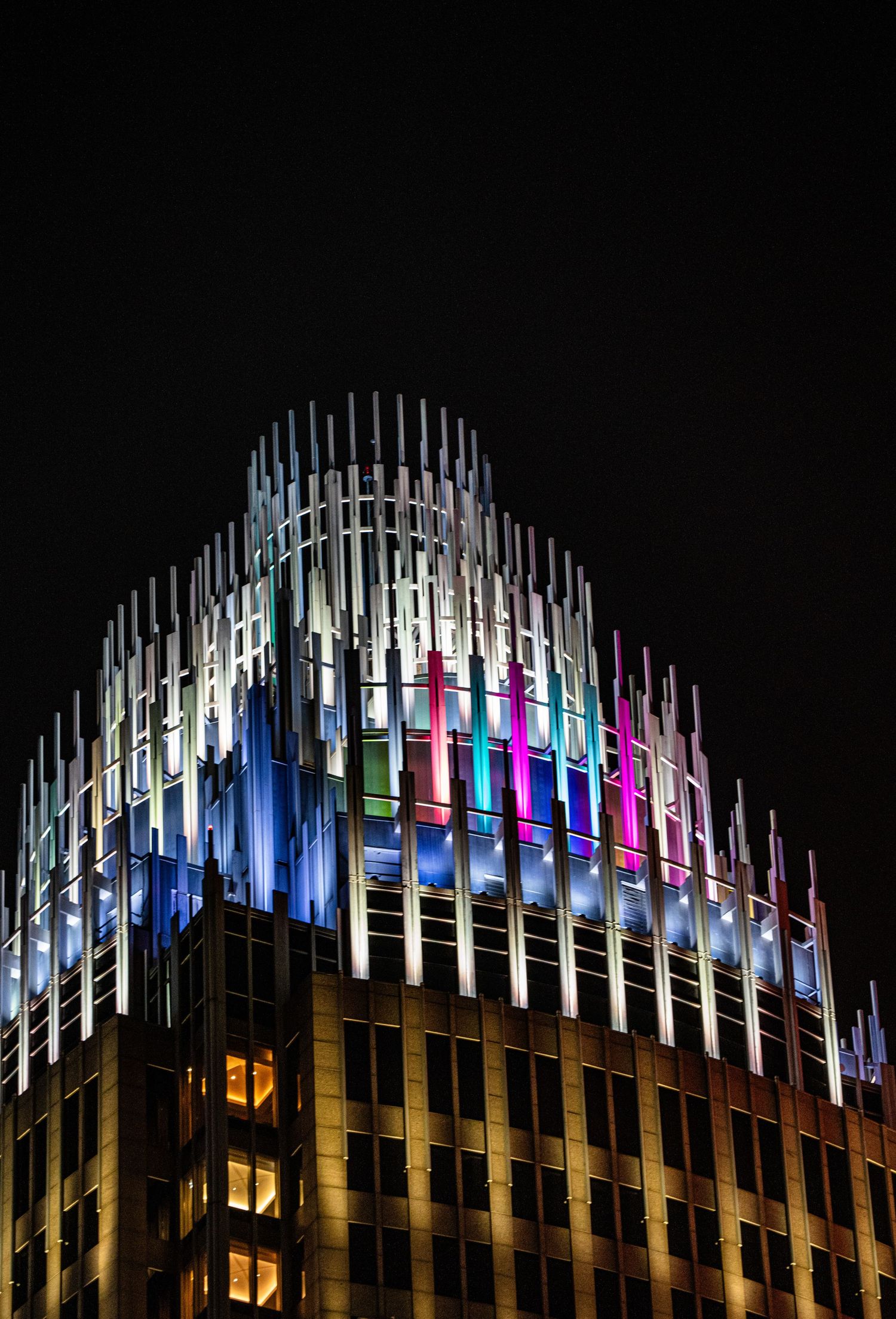 Illuminated architectural crown with multicolored vertical light tubes creating a modern design pattern.