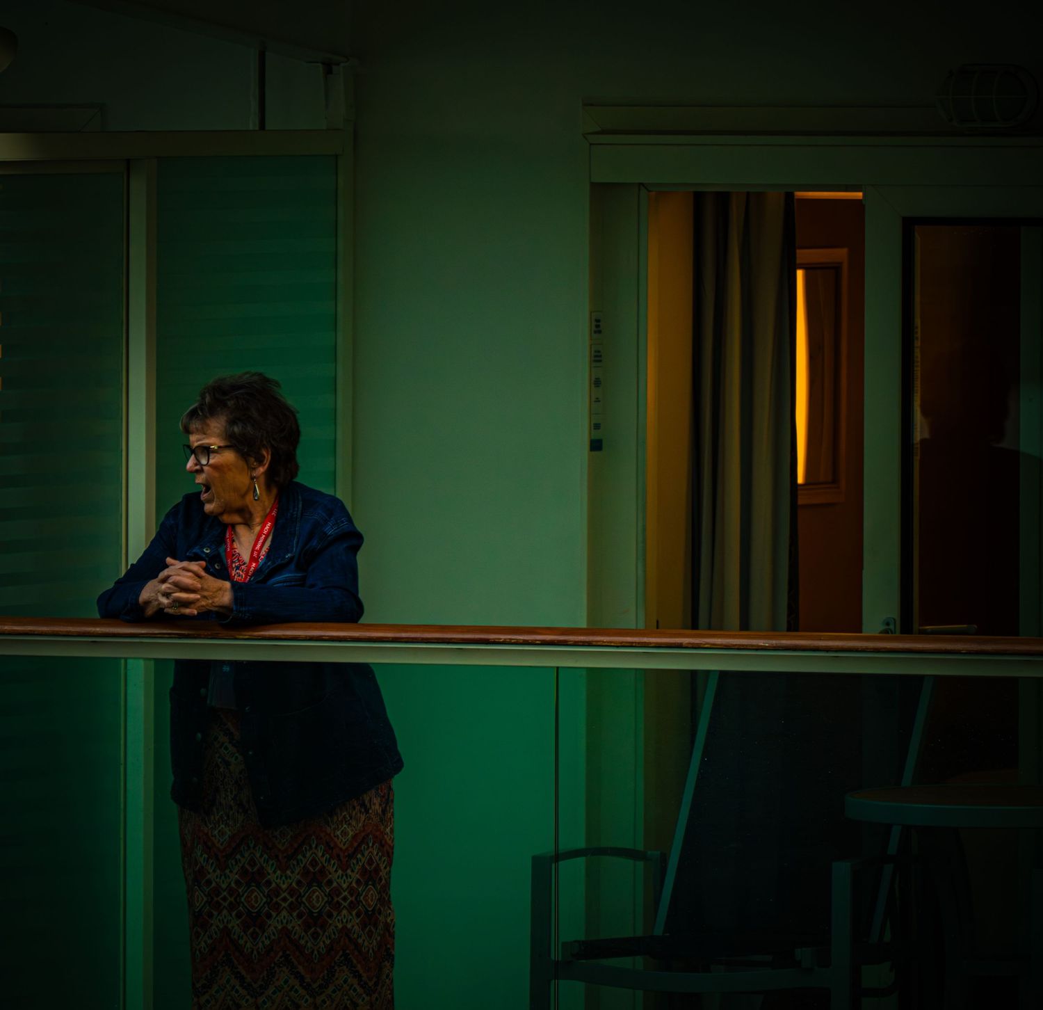A person stands on a dimly lit balcony with green walls and warm interior lighting in the background.