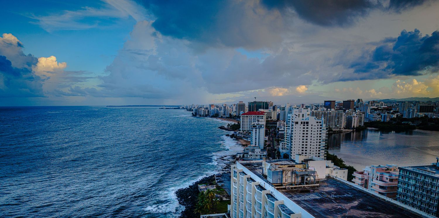 Aerial view of Waikiki Beach with turquoise waters, white sand, and modern beachfront hotels under blue skies.